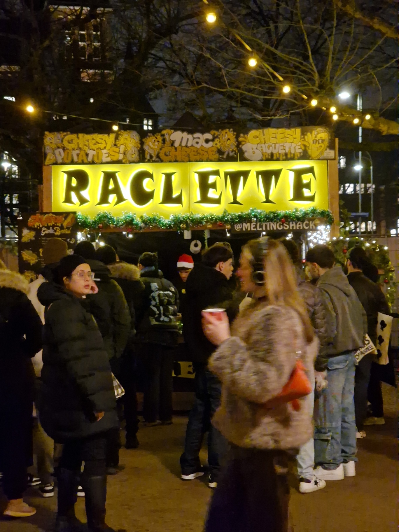 The lit Raclette stall busy with customers at a winter market in the evening