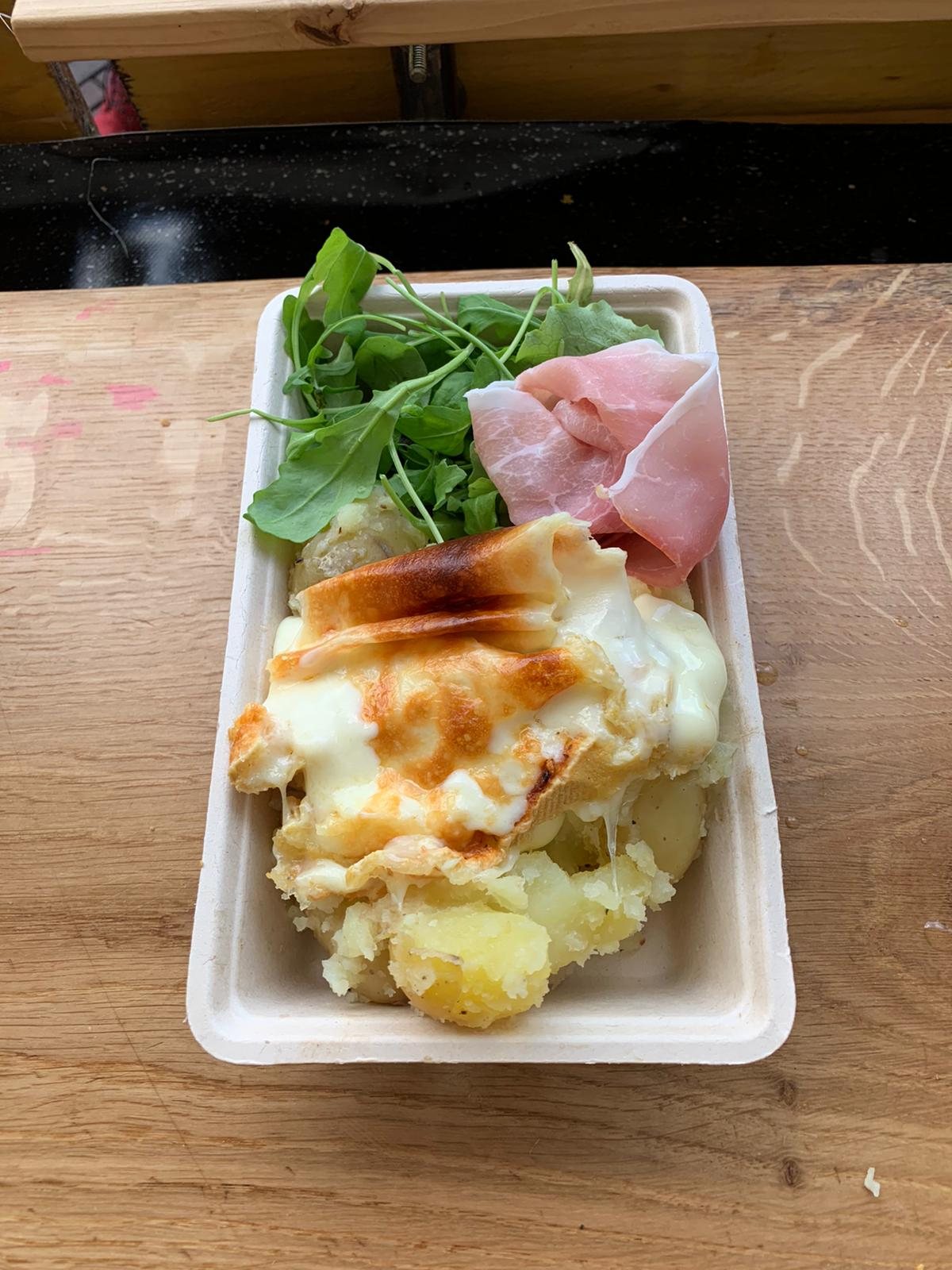Molten raclette cheese being scraped from a half wheel onto crusty bread